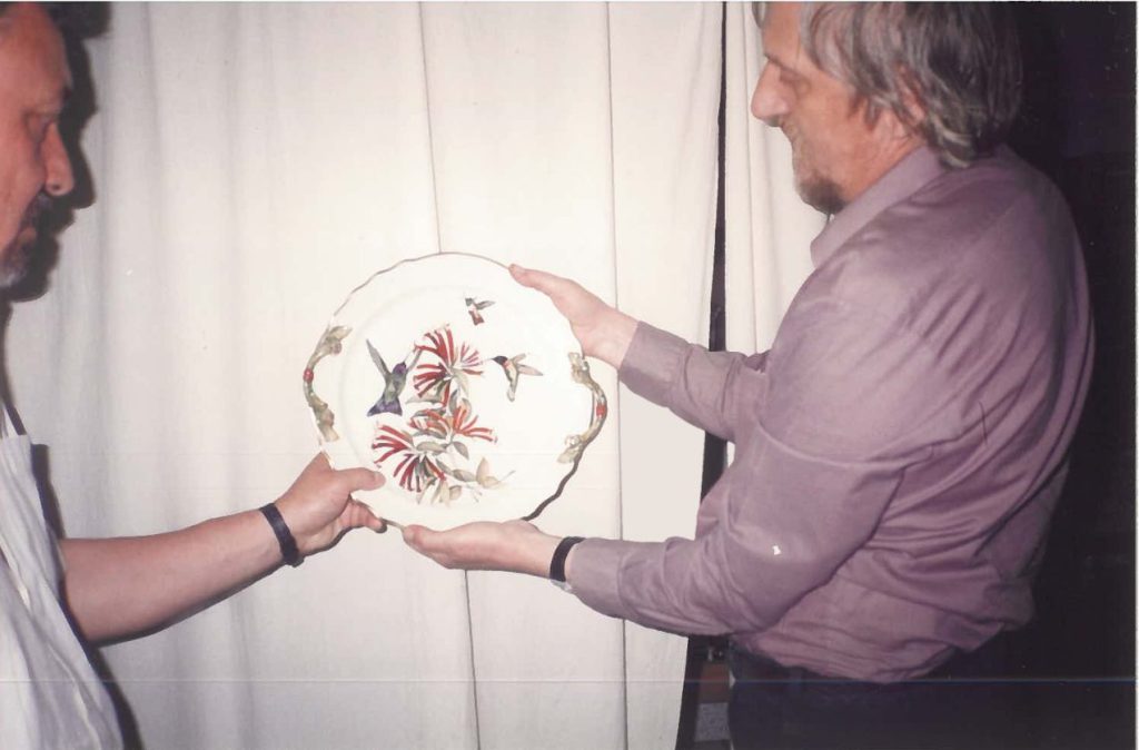 Két ember kezében virágmintás, díszített porcelán tányér, egymásnak átadva.