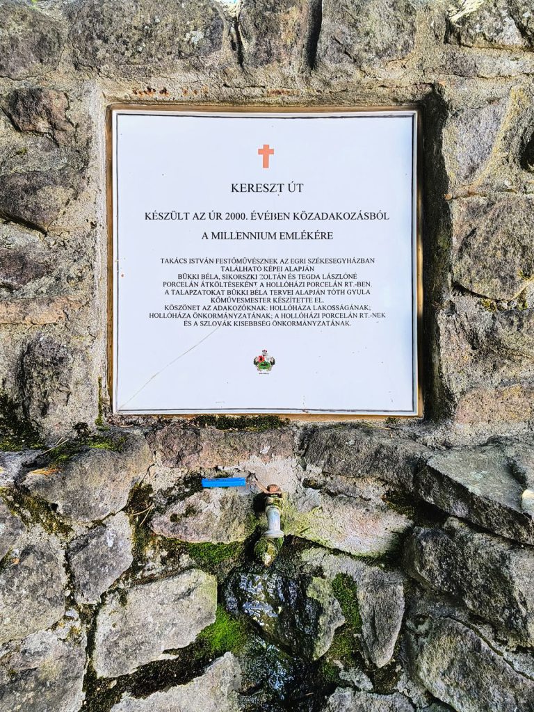 Fehér, aranyszínű keretbe foglalt emléktábla vörös kereszttel, terméskő falban; szövege a keresztút készítőit és az adakozókat sorolja fel.