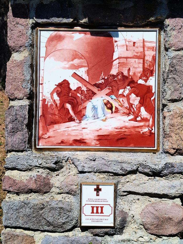 Jézus a kereszt alatt a földre roskad, katonák hajolnak fölé és rángatják. Négyzetes porcelánkép aranyszínű keretben, terméskő pillérbe falazva; alatta kétnyelvű tábla a stáció számával.