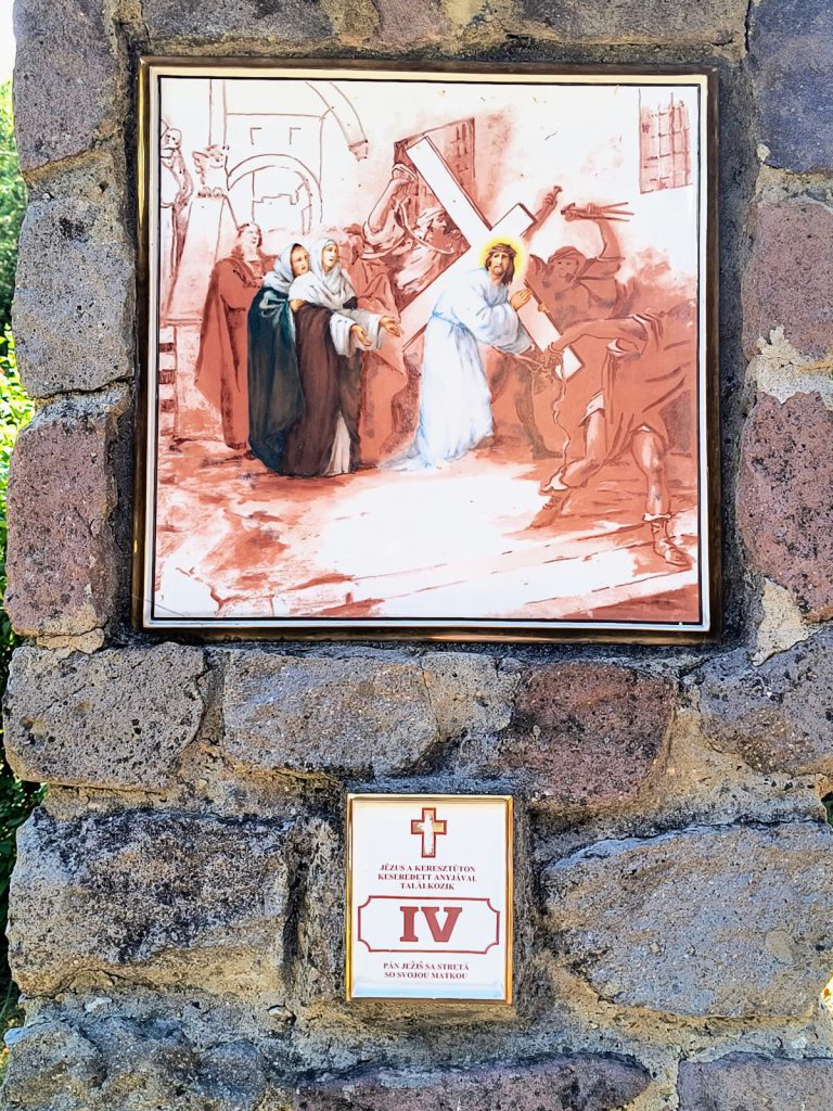 Jézus a keresztet vive az út szélén álló anyjával és a kísérő asszonyokkal találkozik. Négyzetes porcelánkép aranyszínű keretben, terméskő pillérbe falazva; alatta kétnyelvű tábla a stáció számával.