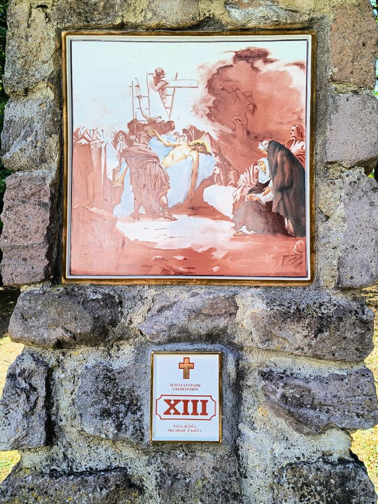 Jézus testét leveszik a keresztről és anyja ölébe fektetik, fölöttük sötét felhő. Négyzetes porcelánkép aranyszínű keretben, terméskő pillérbe falazva; alatta kétnyelvű tábla a stáció számával.