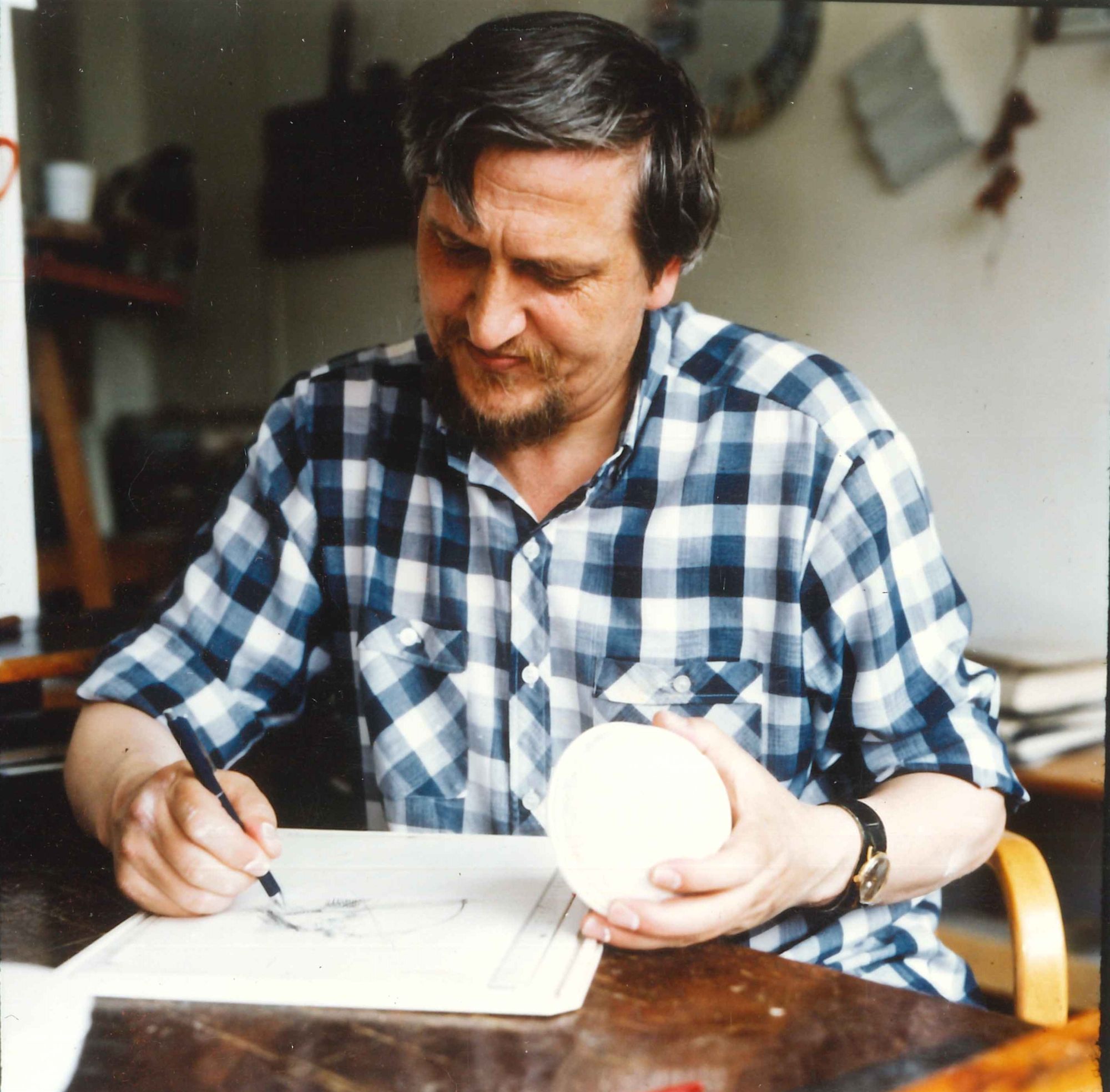 Bükki Béla kockás ingben, íróasztalánál, kezében porcelán tányérral dolgozik.