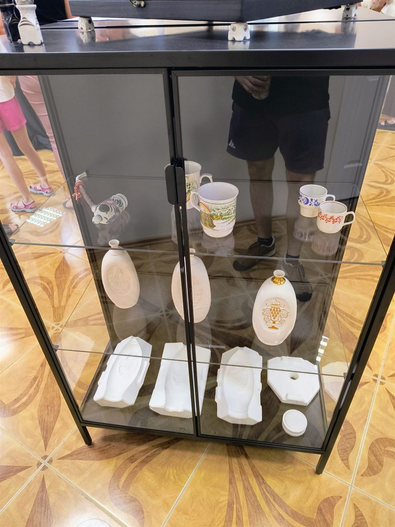 Üvegvitrin polcain porcelán csészék, ovális plakettek és kisméretű figurák.