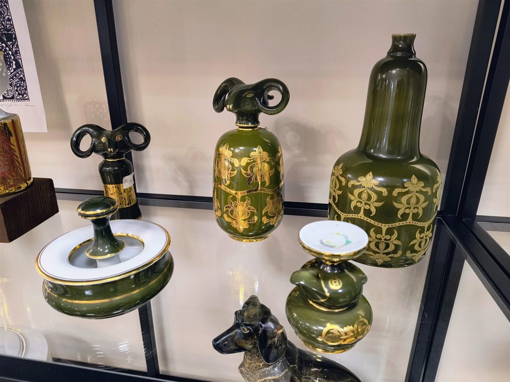 Zöld mázas, aranyozott mintás porcelán palackok és fedeles doboz, mellettük sötét mázas kutyafigura.