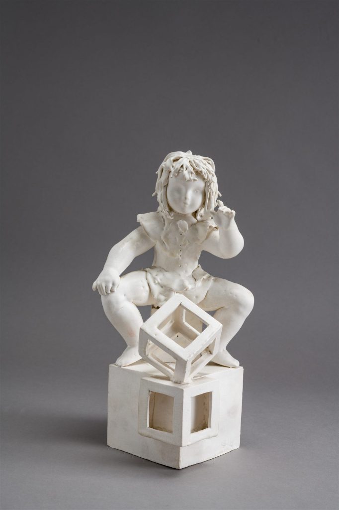 Fehér porcelán akrobatafigura világos talapzaton, szürke háttér előtt.