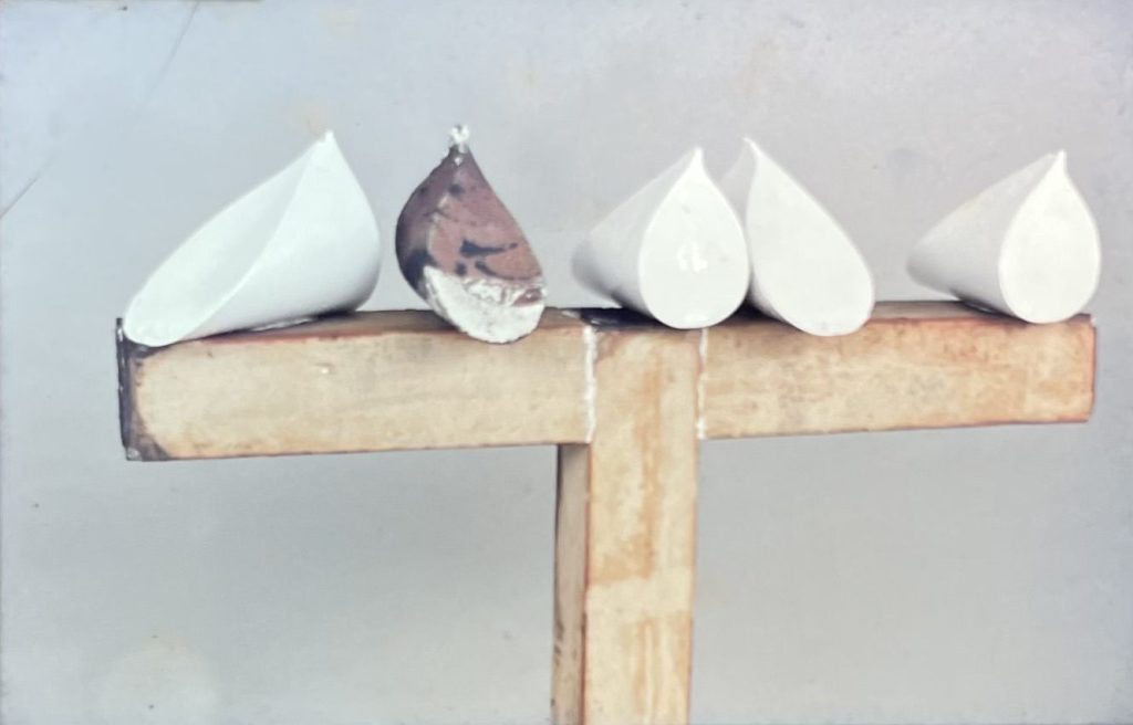 Fehér, csúcsos porcelán galambformák fából ácsolt kereszt alakú tartószerkezeten.