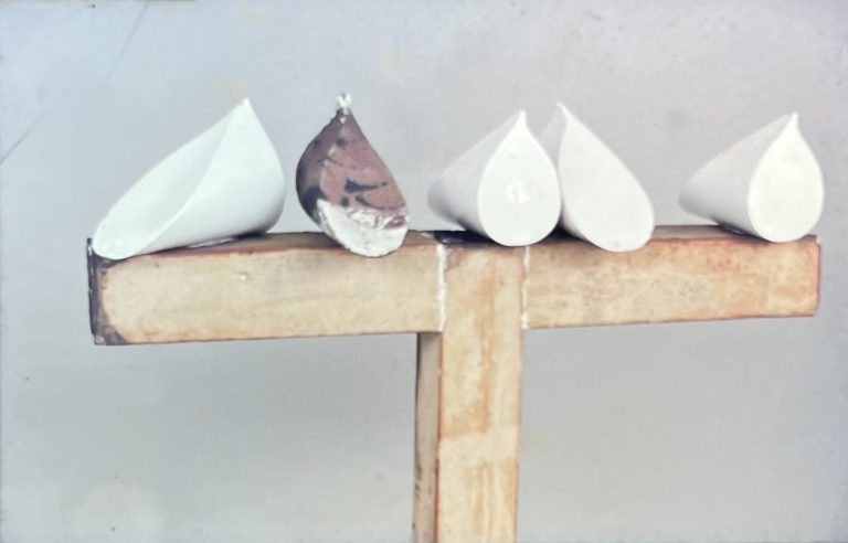 Fehér, csúcsos porcelán galambformák fából ácsolt kereszt alakú tartószerkezeten.