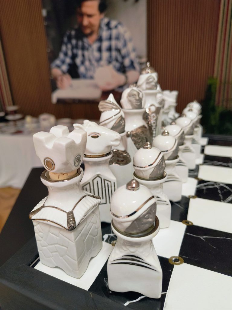Fehér, platinával díszített porcelán sakkfigurák közelről; a bábuk koronája és sisakja levehető dugó, alatta fémgyűrűs nyílás.
